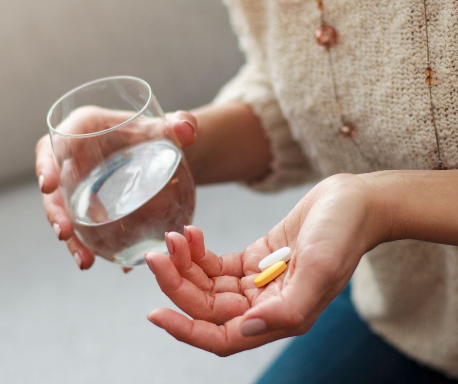 female hands holding vitamins in the palm of one hand and a glass of water in in the other hand.