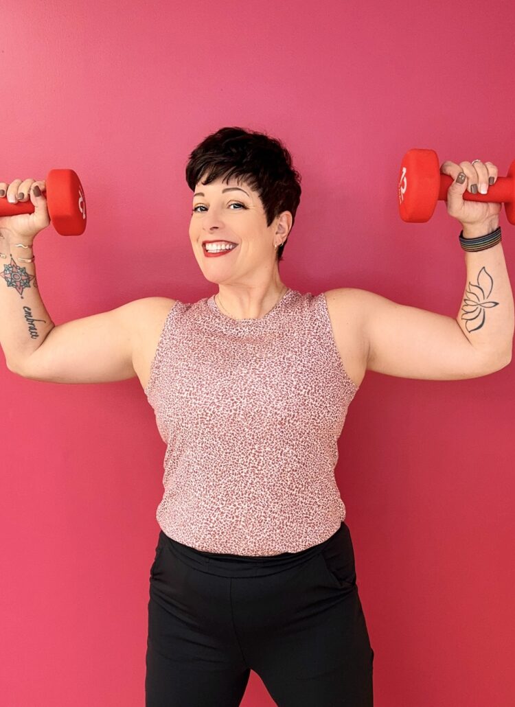 Gretchen Schock holding two dumbbells at shoulder height smiling into the camera