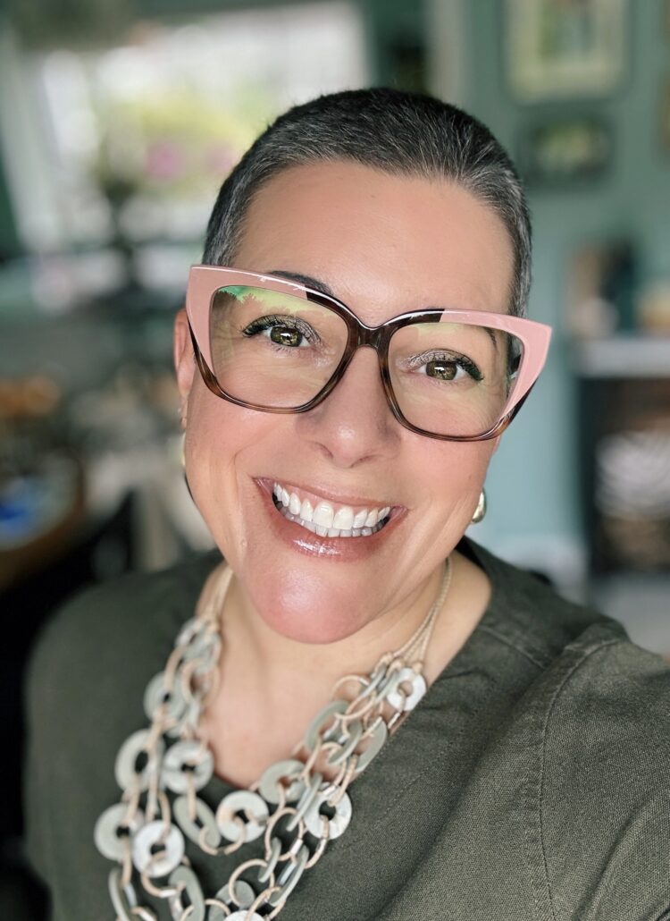 40 something female with pink glasses and a buzzcut smiling at the camera