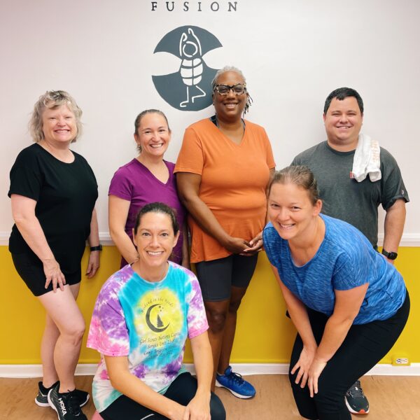 group of men and women over 30 posing in front of the bee yoga fusion logo