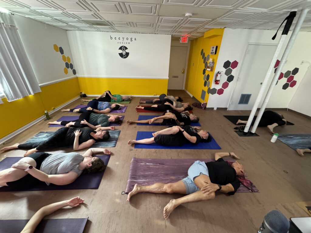 bee yoga fusion yoga class, students are on their backs in a twist