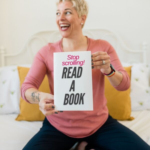 a short haired blonde woman holding a book in front of her that says "stop scrolling! Read a book"