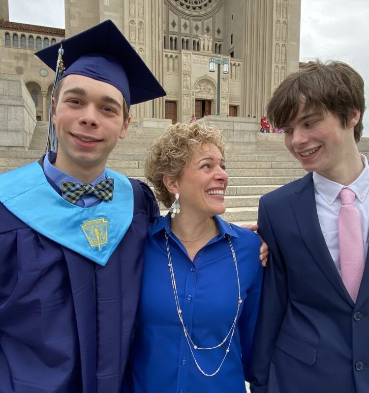 gretchen schock with her two children on graduation day, one is wearing a cap and gown. She is looking into the eyes of the teenager and has tears in her eyes