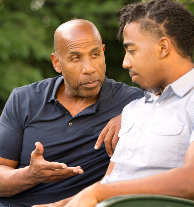 an older man talking to a teenager on a park bench offering advice or words of wisdom