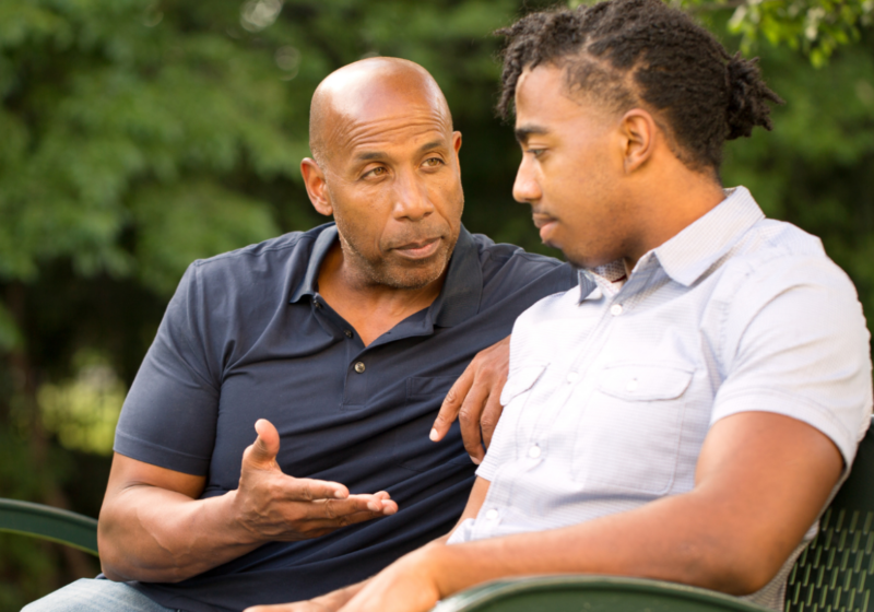 an older man talking to a teenager on a park bench offering advice or words of wisdom