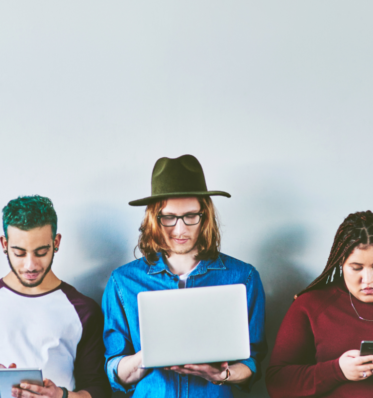 a row of people standing looking at various screens, laptops, phones, tablets etc.