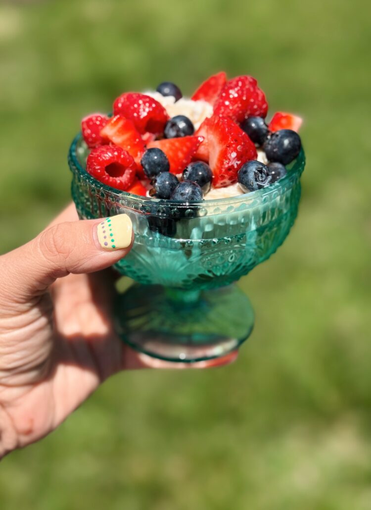 a green glass bowl being held up with vanilla ice cream and beautiful berries with the honey suckle syrup drizzled throughout
