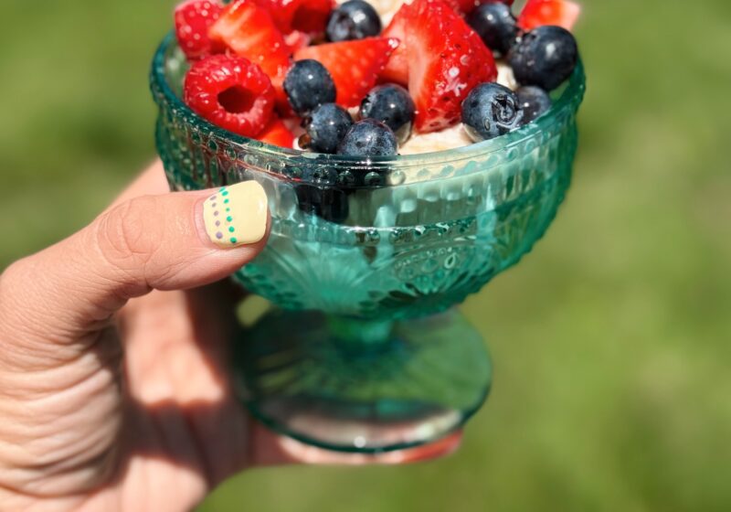 a green glass bowl being held up with vanilla ice cream and beautiful berries with the honey suckle syrup drizzled throughout