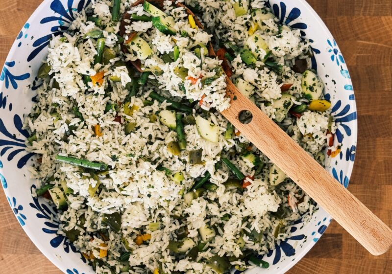 a blue and white bowl on a wooden table, the bowl is filled with the rice dish that the blog post is about. It looks fresh and yummy!