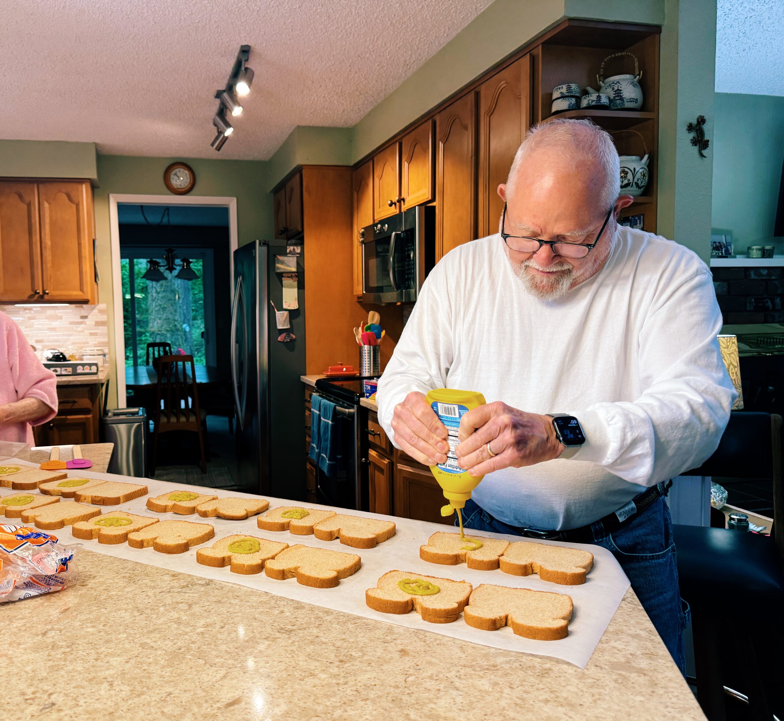 senior man creating an assembly line on the kitchen island to make sandwiches for the unhoused.