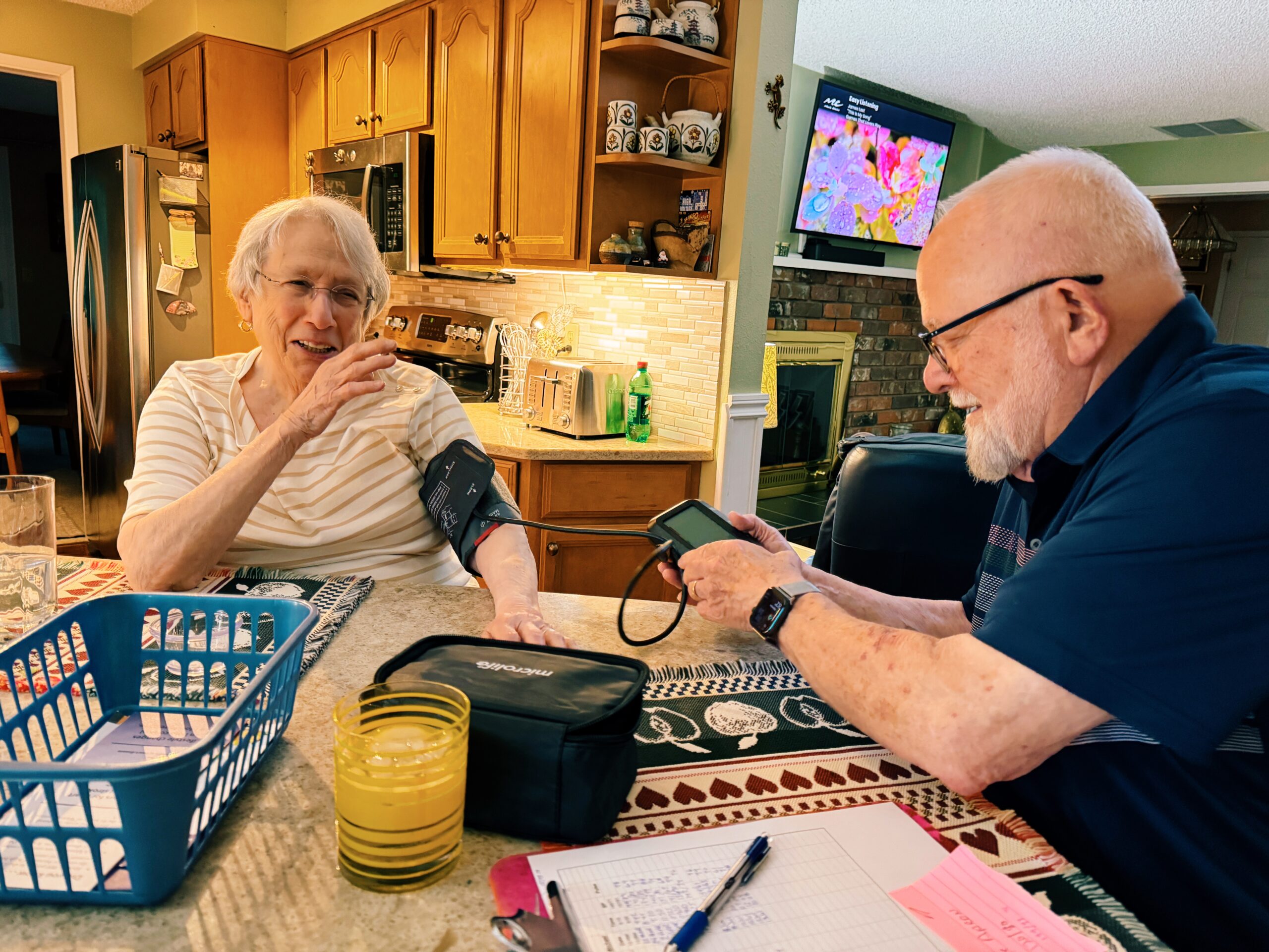 older man taking the blood pressure of a senior aged woman, the woman is laughing and the man is smiling.
