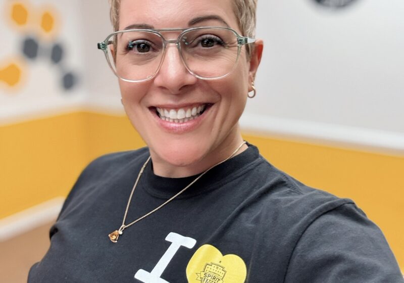 Gretchen Schock a woman in her late 4os wearing glasses and smiling into the camera. She has a short pixie haircut and a t-shirt that says "I heart DC"