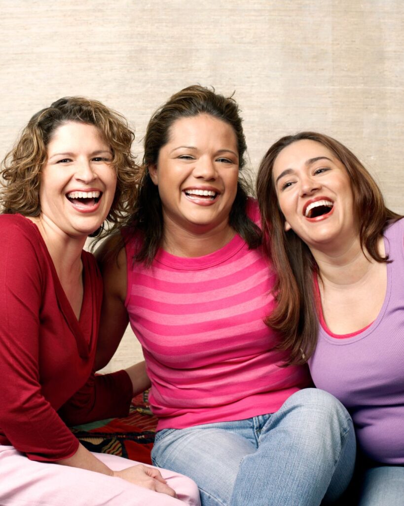 three women sitting near each other on a sofa with big smiles